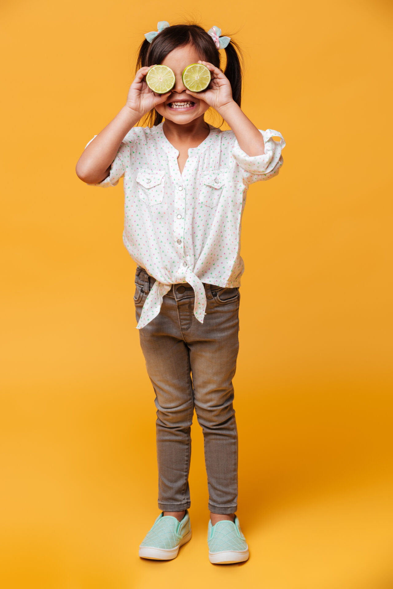 Une enfant souriante s'amuse avec un orange coupée en guise de jumelles